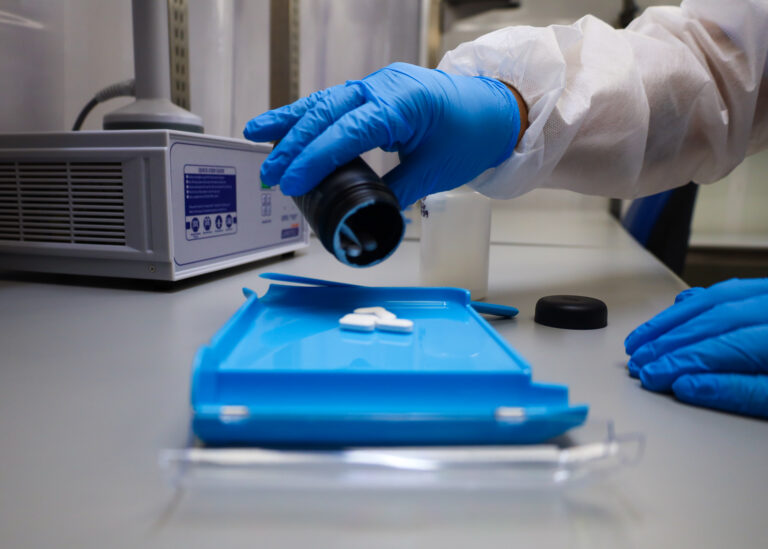 Nutraceutical Contract Packaging and Sample Fulfillment 3 Gloved hands dispensing white supplement tablets from a bulk bottle onto a counting tray during sample pack assembly